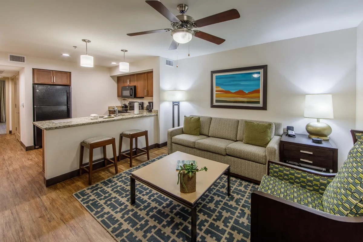The image showcases the inviting interior of a Scottsdale villa, with a cozy sofa and coffee table set in a spacious, open-plan living area. The stylish kitchen area is visible in the background, perfect for preparing meals, while tasteful southwestern artwork and warm lighting create a welcoming ambiance. The scene suggests relaxation, socializing, and quality time together, ideal for families or couples.