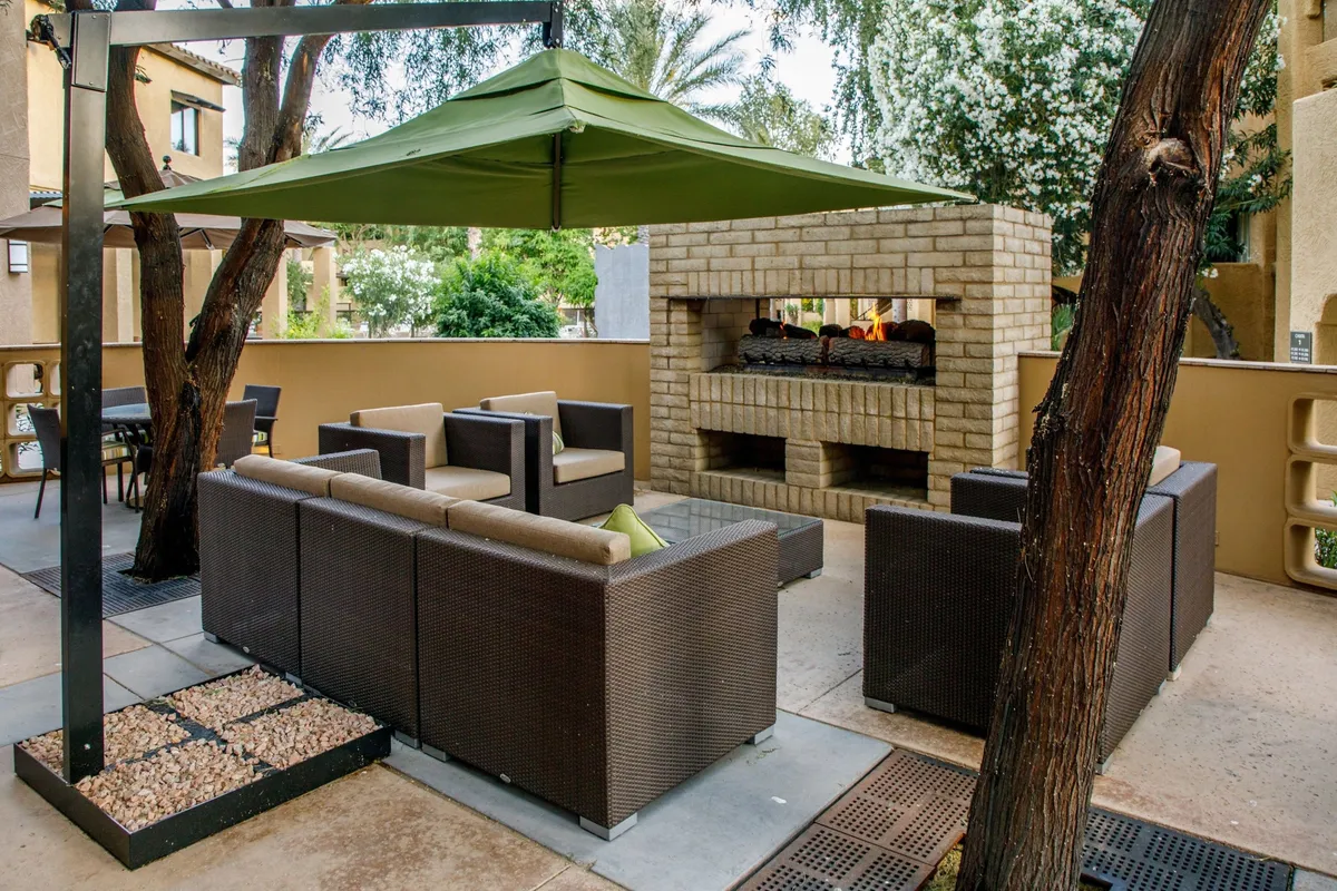 An inviting outdoor seating area is shown beneath a green canopy, with a cozy fireplace as a focal point. The space encourages socializing, relaxing, and possibly dining al fresco, capturing the essence of relaxing evenings after active, adventure-filled days.