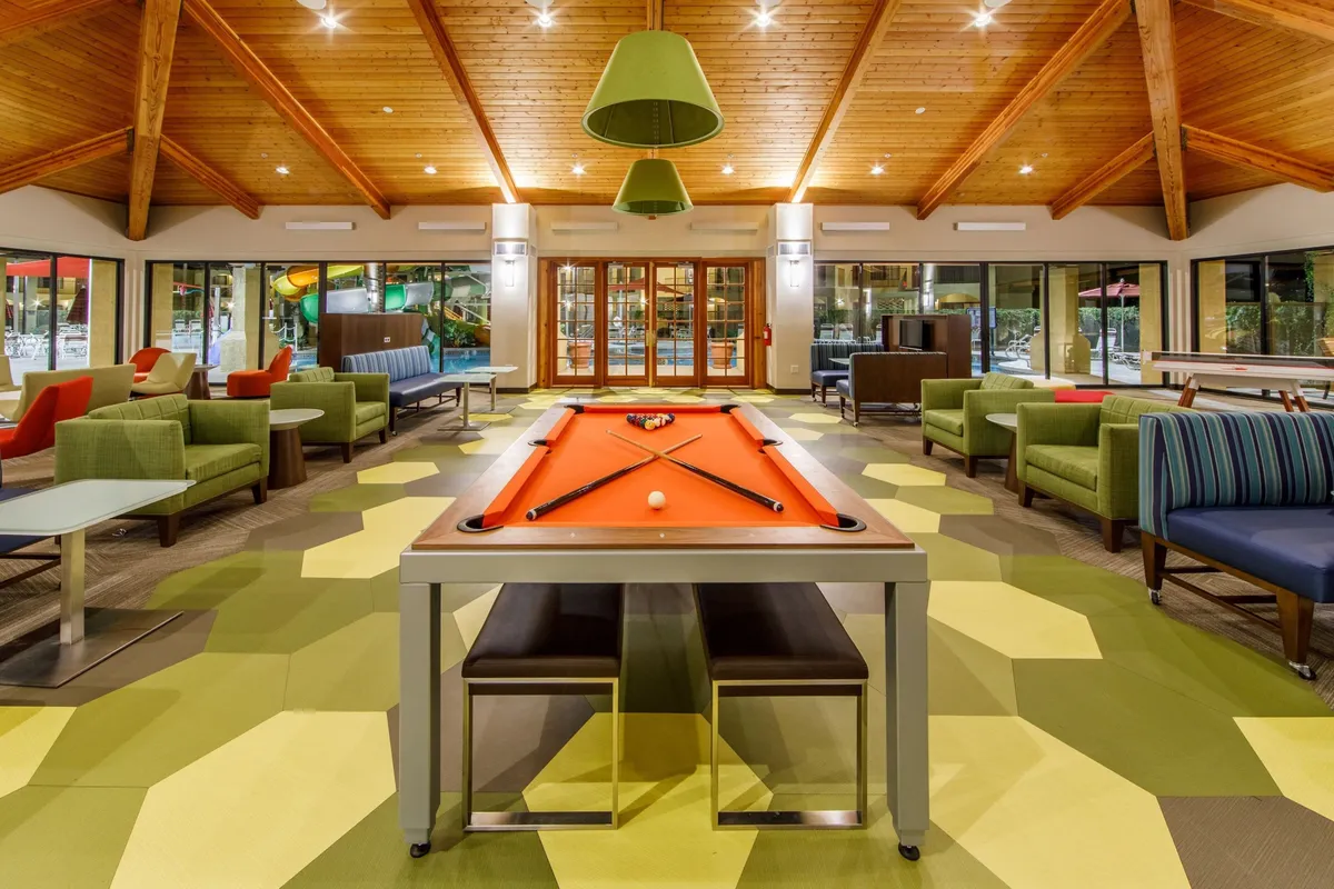 A cheerful interior shot of the family activity center, highlighting a pool table, bright seating, and large windows letting in natural light. The space invites friendly competition, group activities, and relaxation for all ages.